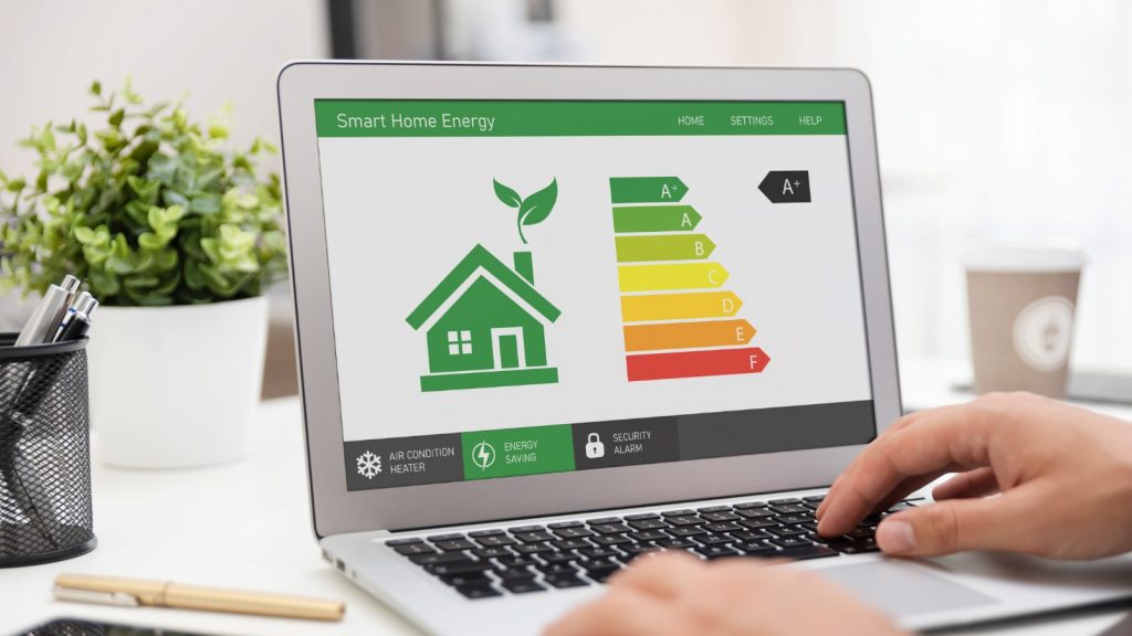 Pantalla de laptop mostrando una aplicación de eficiencia energética para el hogar con una escala de consumo energético y un icono de casa con una hoja verde.